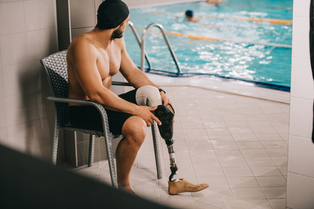 Athletic sportsman with artificial leg sitting on chair at indoor swimming poolの写真素材