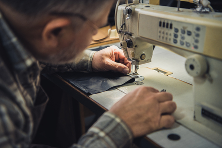 Partial view off male handbag craftsman working on sewing machine at studioの写真素材