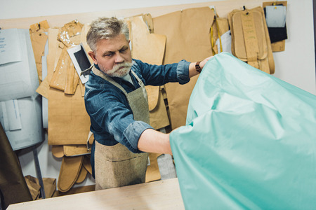Mature male handbag craftsman putting fabric on working table at studioの写真素材