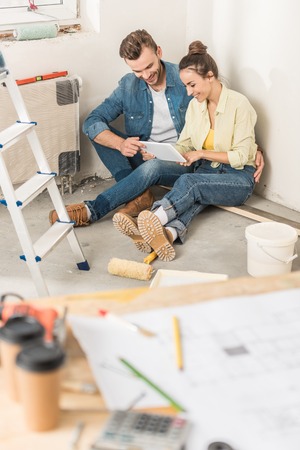 High angle view of smiling young couple using digital tablet while sitting on floor during house repairの写真素材