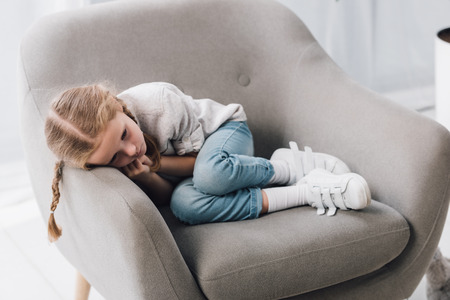 Sad little child lying in armchair aloneの写真素材