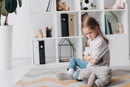Depressed little child sitting on floor with teddy bearの写真素材
