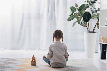 Rear view of little child sitting on floor with wooden blocks and looking awayの写真素材