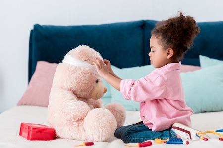 Little African american child in pink jacket playing the doctor  with teddy bearの写真素材
