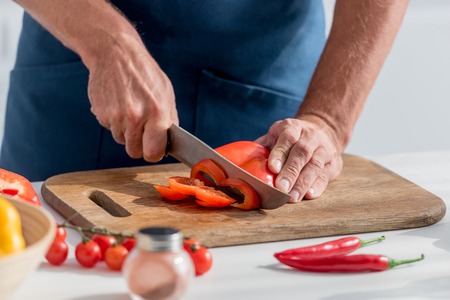 Partial view of man cutting red bell pepper for salad