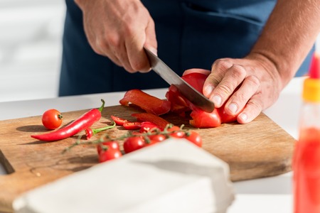 Close up view of male hands cutting chili peppers on chopping boardの写真素材