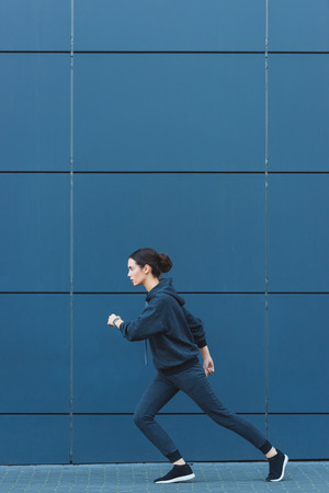 Active adult sportswoman jogging in sportswear near buildingの写真素材
