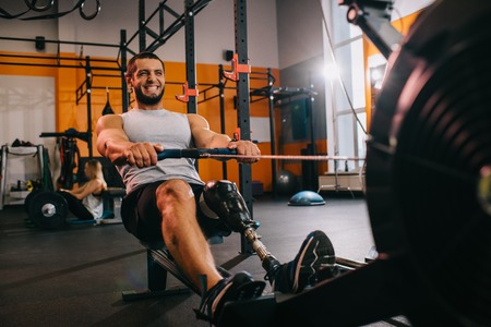 A handsome young sportsman with artificial leg working out with rowing machine at gymの写真素材
