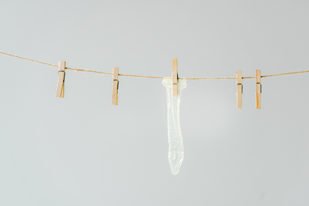 A row of wooden clothespins with white condom hanging on clothesline isolated on greyの写真素材