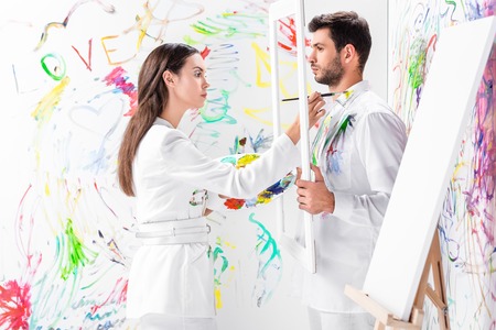 Adult man holding white frame while woman painting clothesの写真素材