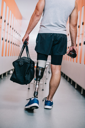 Cropped shot of sportsman with artificial leg standing at gym changing room with bottle and bagの写真素材