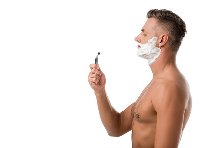 Side view of adult man with shaving foam on face holding razor isolated on whiteの写真素材