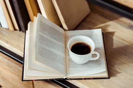 Close up of open book with cup of coffee on bookshelf
