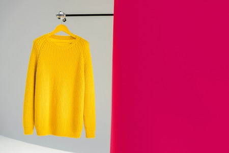 Knitted yellow sweater on hanger on pink and grey backgroundの写真素材