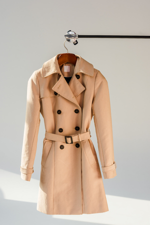 Beige trench coat with belt and black buttons on hangerの写真素材