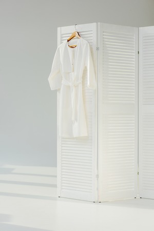 Elegant white dress hanging on wooden room dividerの写真素材
