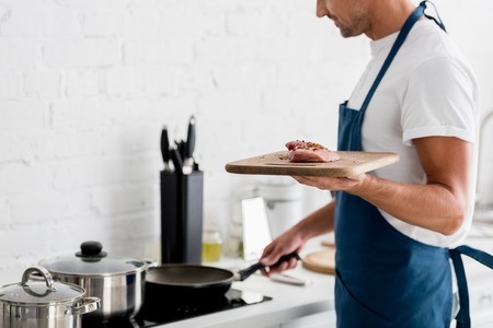 Adult man standing on kitchen with pan and fresh steak