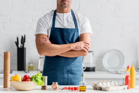 Man in apron standing on kitchen with crossed armsの写真素材