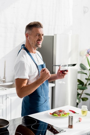 Smiling man with glass of wine listening to music at kitchen