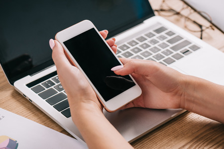 Cropped shot of businesswoman using smartphone at workplace with laptop and papersの写真素材