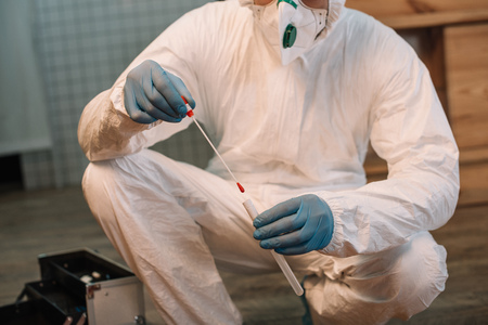 Cropped view of forensic investigator in latex gloves taking blood samples at crime scene