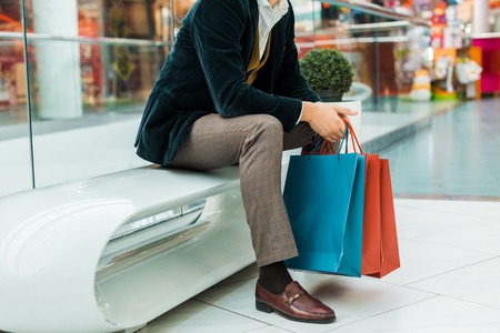 Cropped view of stylish man holding shopping bags and sitting in mallの写真素材