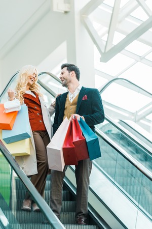 Happy stylish couple with shopping bags standing on escalatorの写真素材