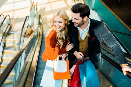 Elegant smiling couple with shopping bags standing on escalatorの写真素材