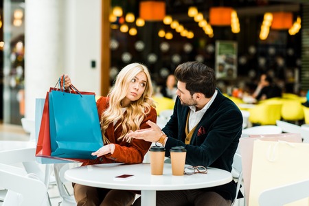 Confused woman showing shopping bags to man in cafe in shopping mallの写真素材