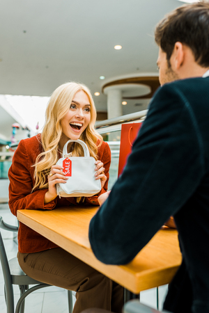 Excited beautiful girl showing bag with sale tag to boyfriendの写真素材