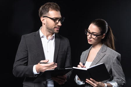 confident business people with clipboard having conversation isolated on blackの写真素材