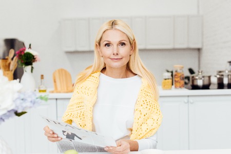 attractive blonde mature woman reading newspaper at kitchen