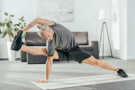 sporty adult man balancing and stretching on yoga mat at homeの写真素材
