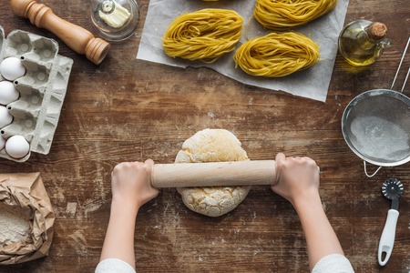 top view of female hands forming dough with rolling pin on wooden tableの写真素材