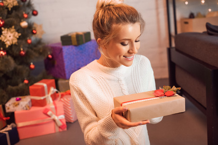 happy blonde young woman sitting and holding present at christmas timeの写真素材