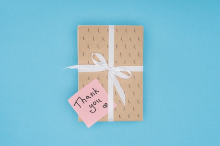 top view of gift box with sticky note with thank you lettering isolated on blue background