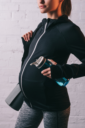 Cropped view of athletic pregnant woman with sportive mat and bottle of waterの写真素材