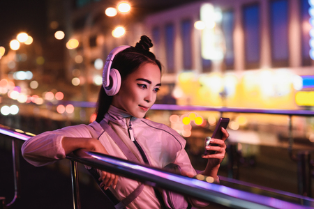 attractive asian girl listening music with smartphone on street with neon light in evening, city of future conceptの写真素材