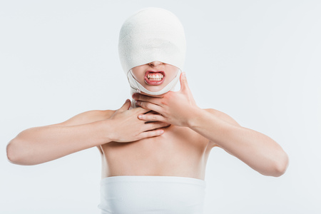 angry woman with bandages on head after plastic surgery touching throat isolated on whiteの写真素材