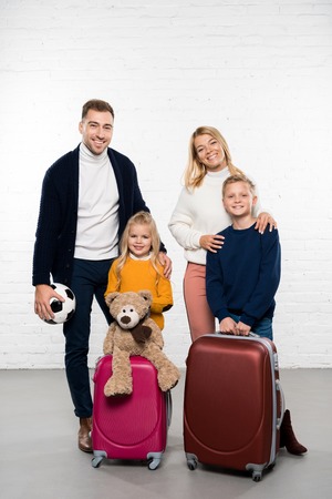 happy family ready to go on winter holidays with luggage looking at camera on white backgroundの写真素材