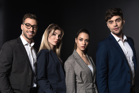 group of confident business people looking at camera together while standing in row isolated on blackの写真素材