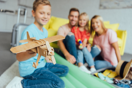 boy playing with toy wooden airplane with family having fun on background and packing for summer holidayの写真素材