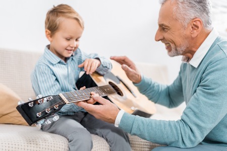 happy mature man teaching grandson playing on acoustic guitar at homeの写真素材