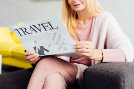 close up of mature woman sitting on sofa and reading travel newspaperの写真素材