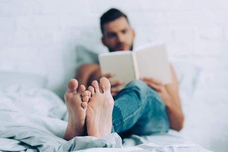 selective focus of man reading book in bedroom at home