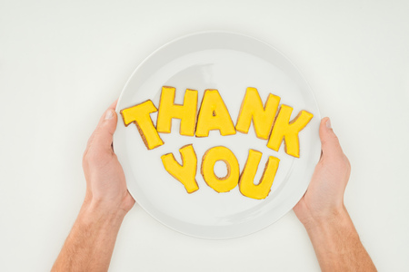 Cropped view of male hands holding white plate with thank you lettering made of cookies isolated on white backgroundの写真素材