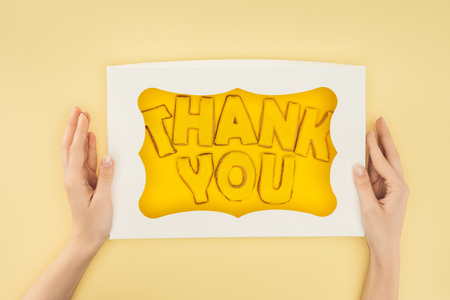 cropped person holding square-shaped cake in box with thank you lettering isolated on yellow backgroundの写真素材