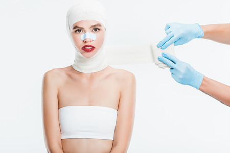 surgeon hands taping up woman after plastic surgery isolated on whiteの写真素材