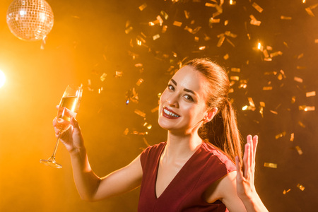 emotional young woman with champagne glass under falling confetti, christmas conceptの写真素材