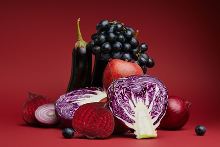 close-up view of sliced cabbage, beetroot, onions, eggplants, apple and grapes on red